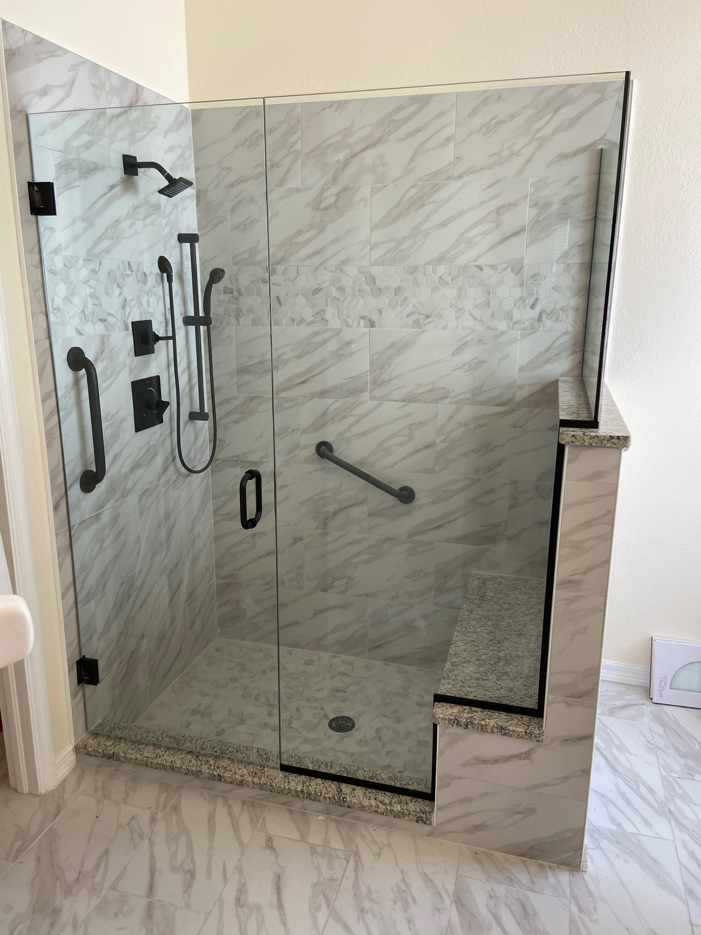 Frameless hinged shower door with matte black hardware and marble tile — Naples install